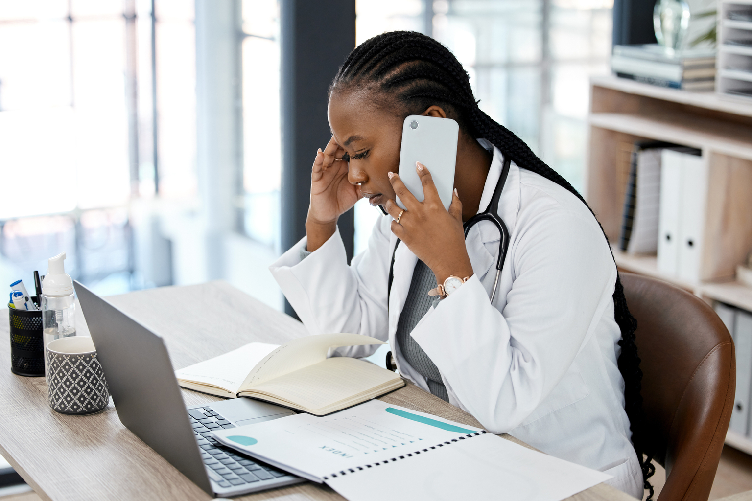 Female african american doctor having a stressful medical consulting discussion on a phone call in a hospital clinic office