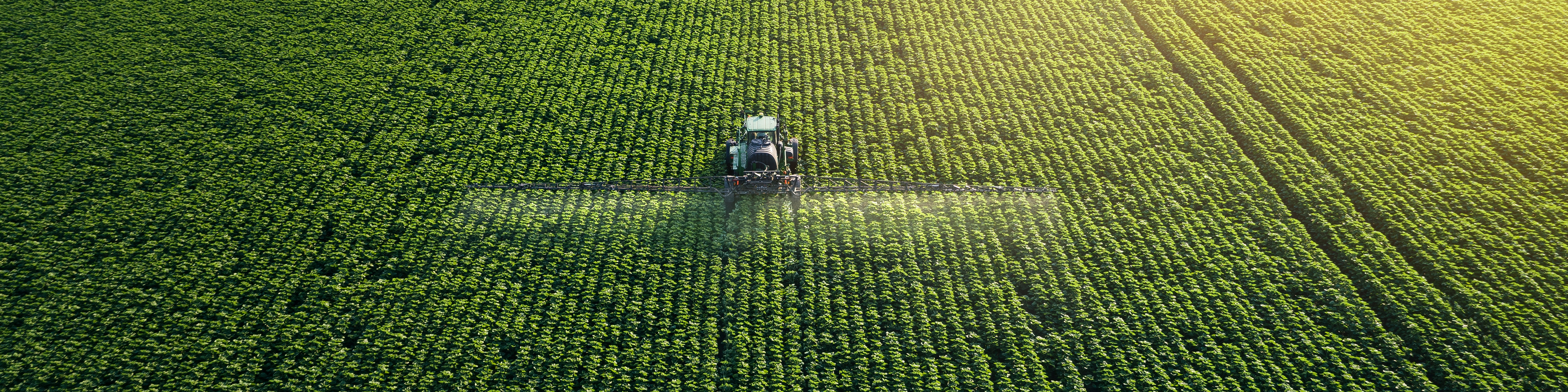 Taking care of the Crop. Aerial view of a Tractor fertilizing a cultivated agricultural field.