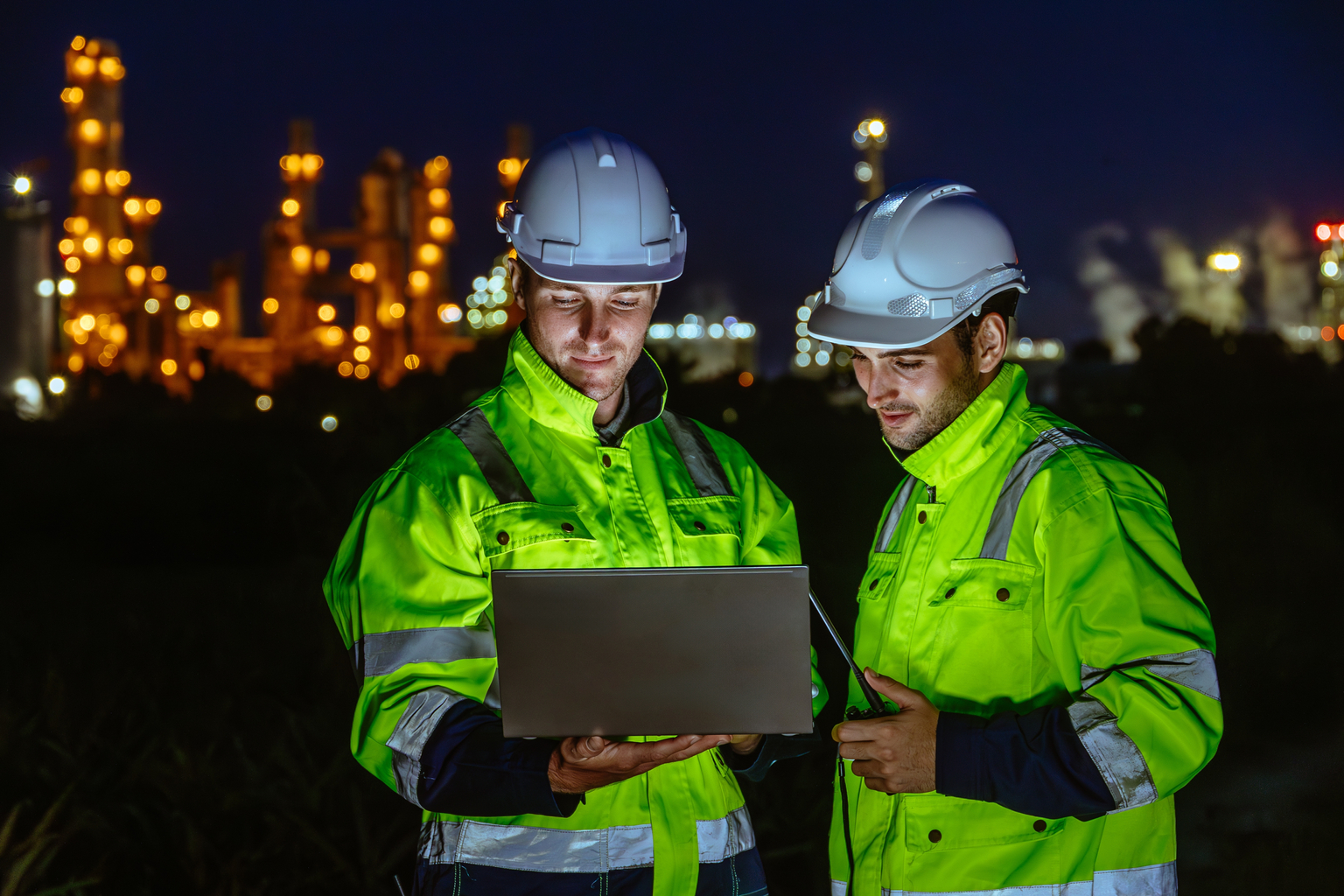 Night shift engineer oil and gas refinery service team worker hard work in petroleum industry plant light blur background.