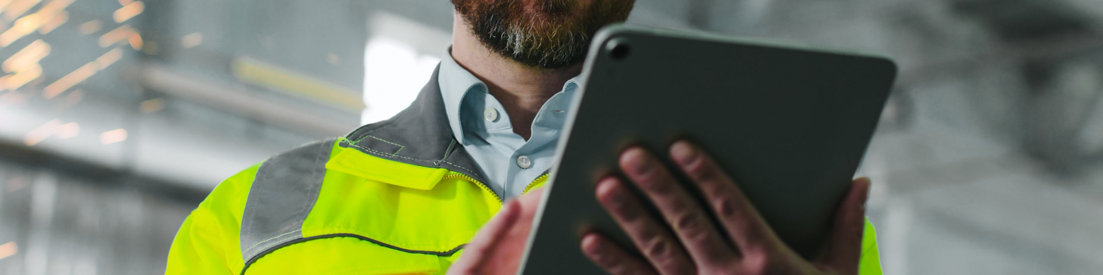 Mature bearded man on construction site. Engineer in uniform and glasses holds tablet background of workflow. An employee notes something in his gadget in workshop. Diversity of proffesions.