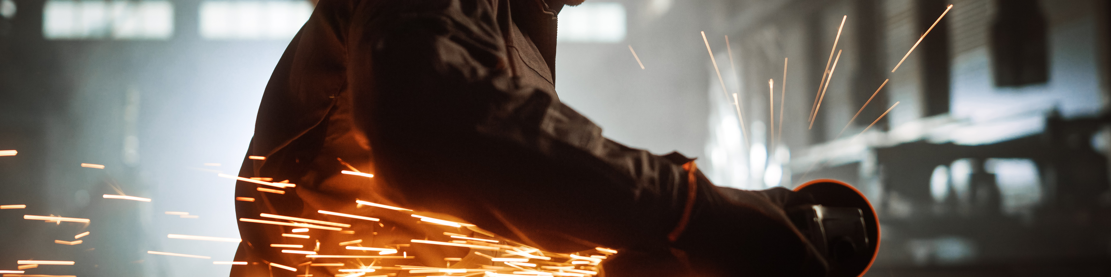 Heavy Industry Engineering Factory Interior with Industrial Worker Using Angle Grinder and Cutting a Metal Tube. Contractor in Safety Uniform and Hard Hat Manufacturing Metal Structures.