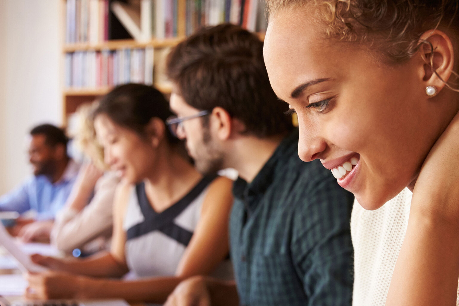 Multiple professionals in a library space reading print materials and using TeamMate on their computers.