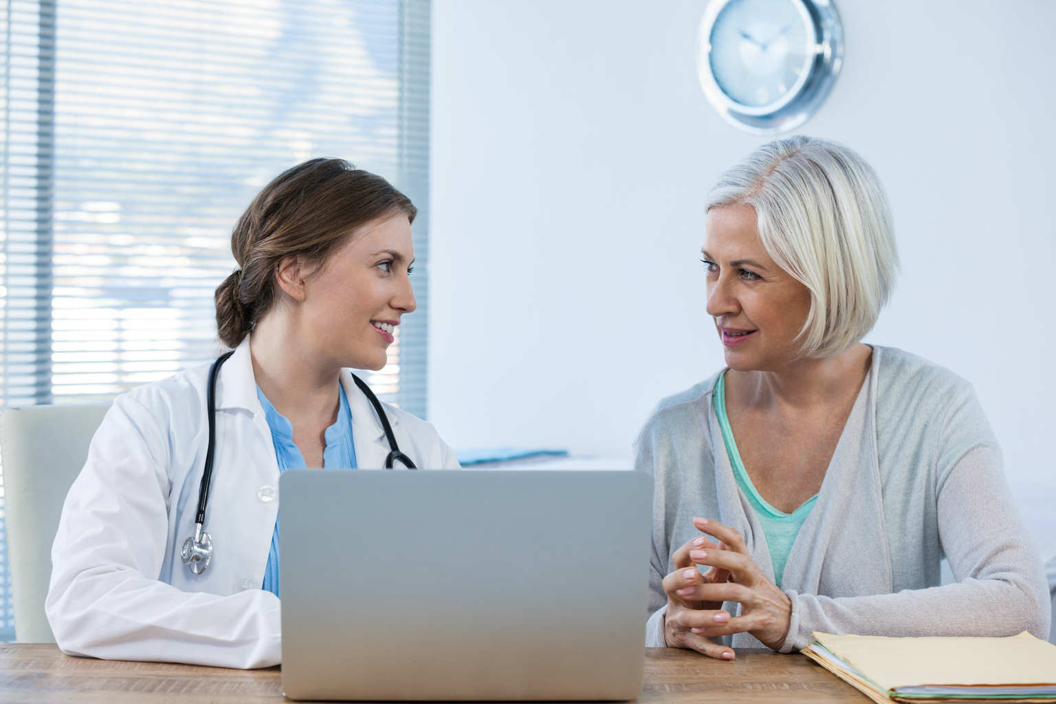 Female doctor interacting with her middle age female patient with a laptop during consultation