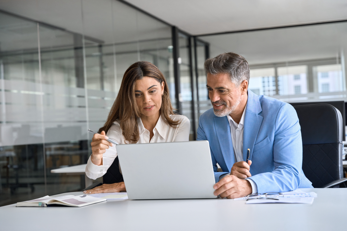 Two busy happy middle aged professional business man and woman executive leaders team using laptop working on computer at work desk