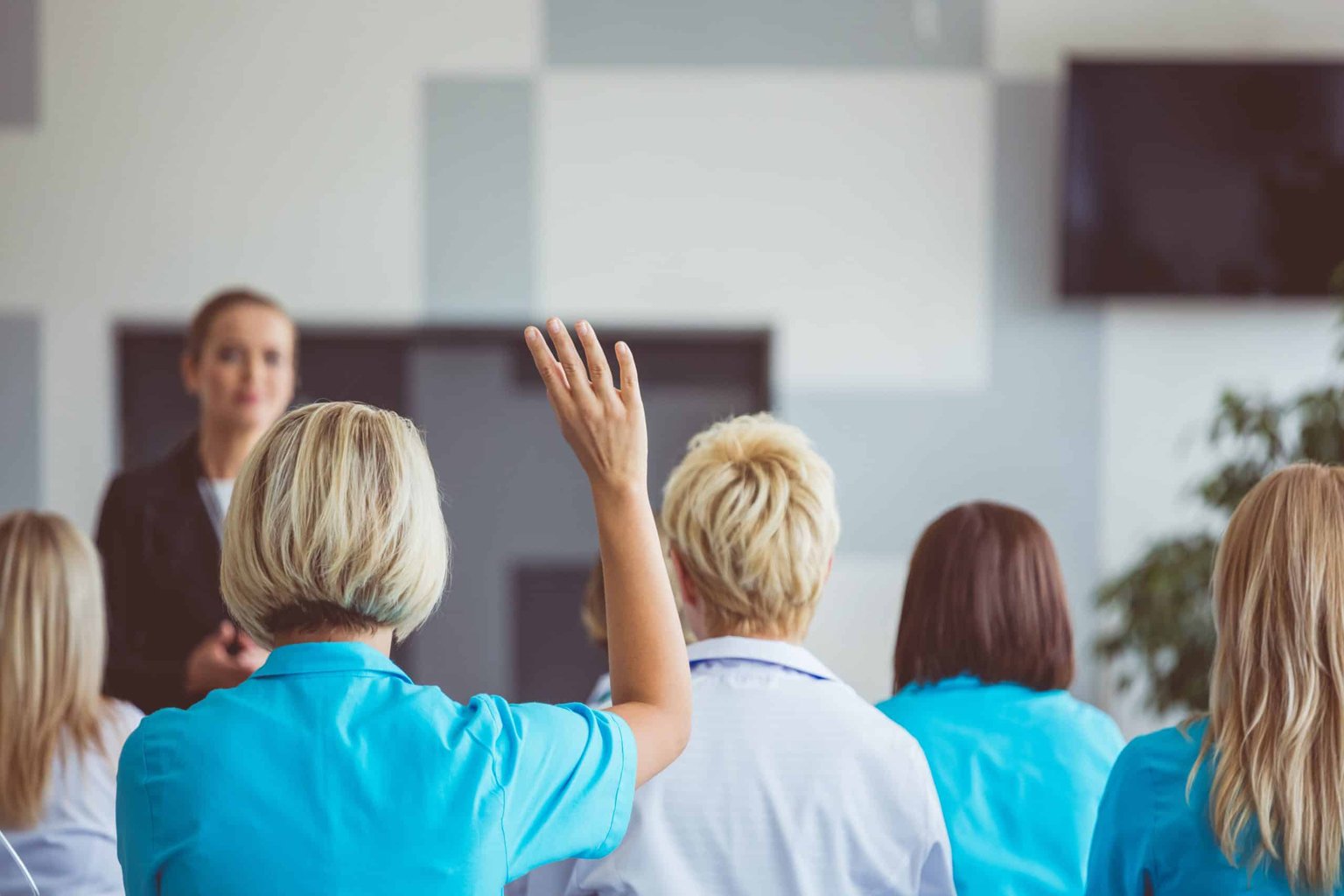 Healthcare professionals in a classroom, woman with hand raised