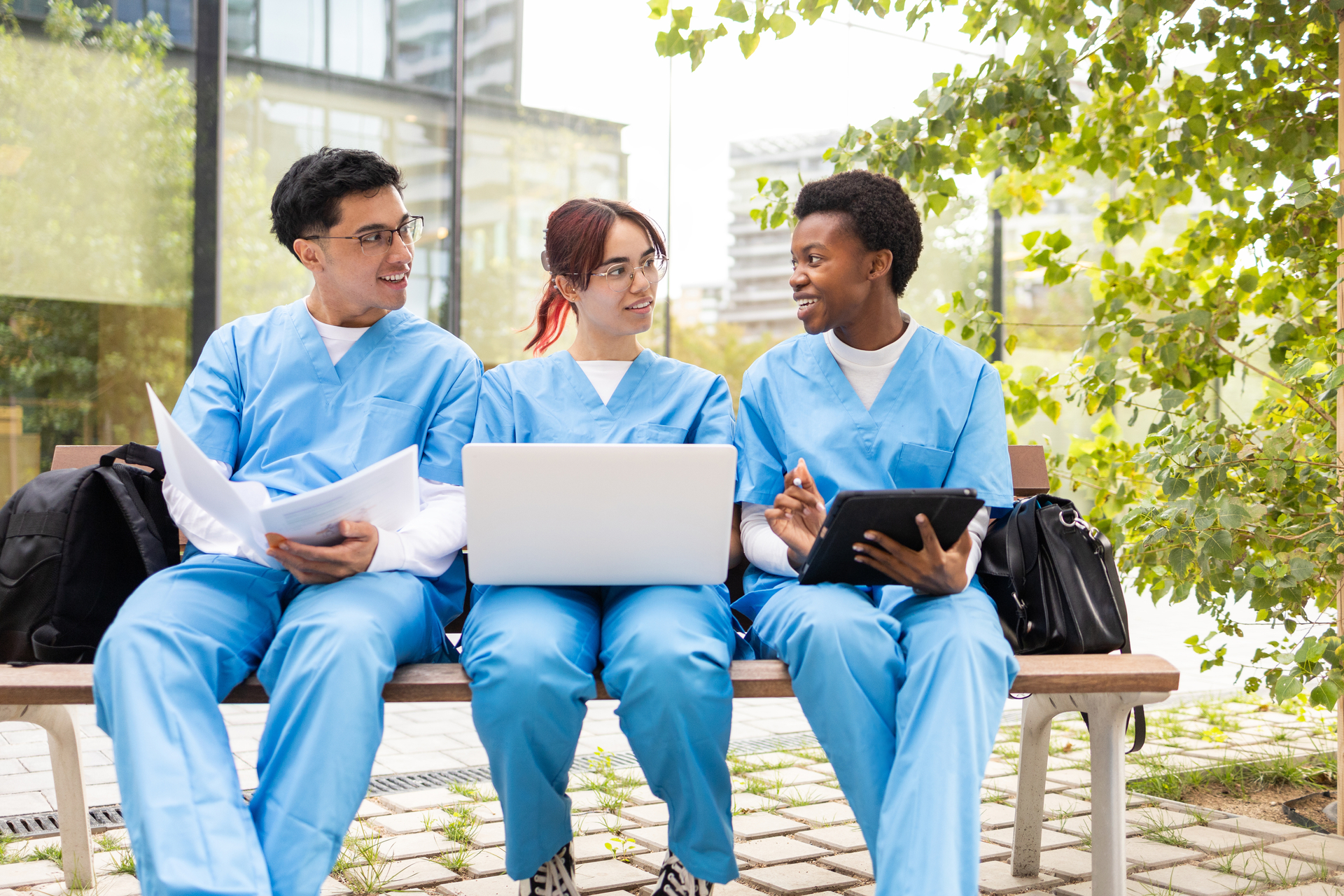 Three nursing students studying together on bench in sunny courtyard