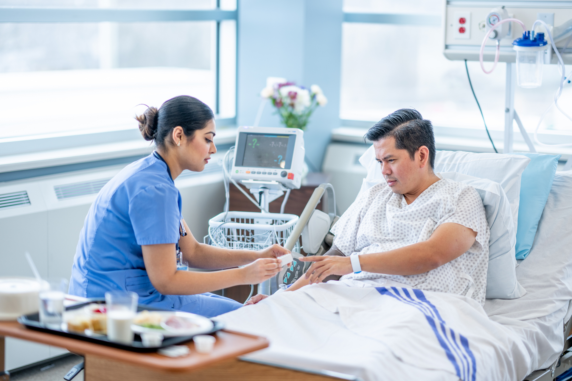 Nurse at patient bedside helping him to put on heart monitor