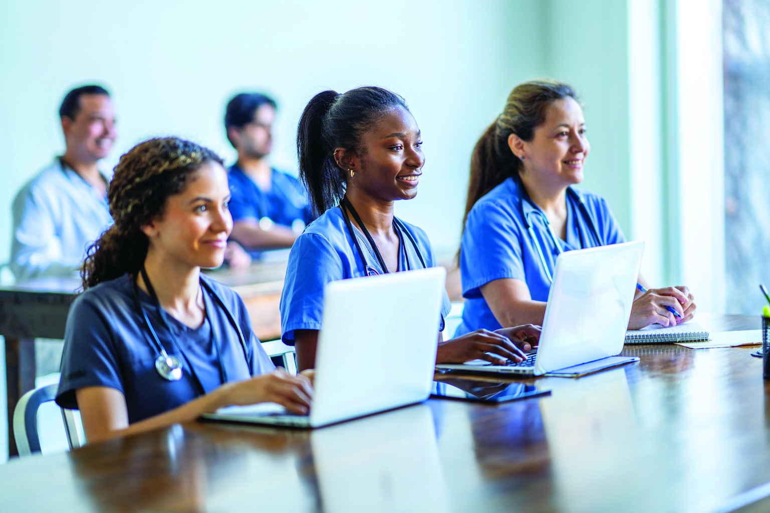 Three medical students in a classroom using laptops to take notes during lecture