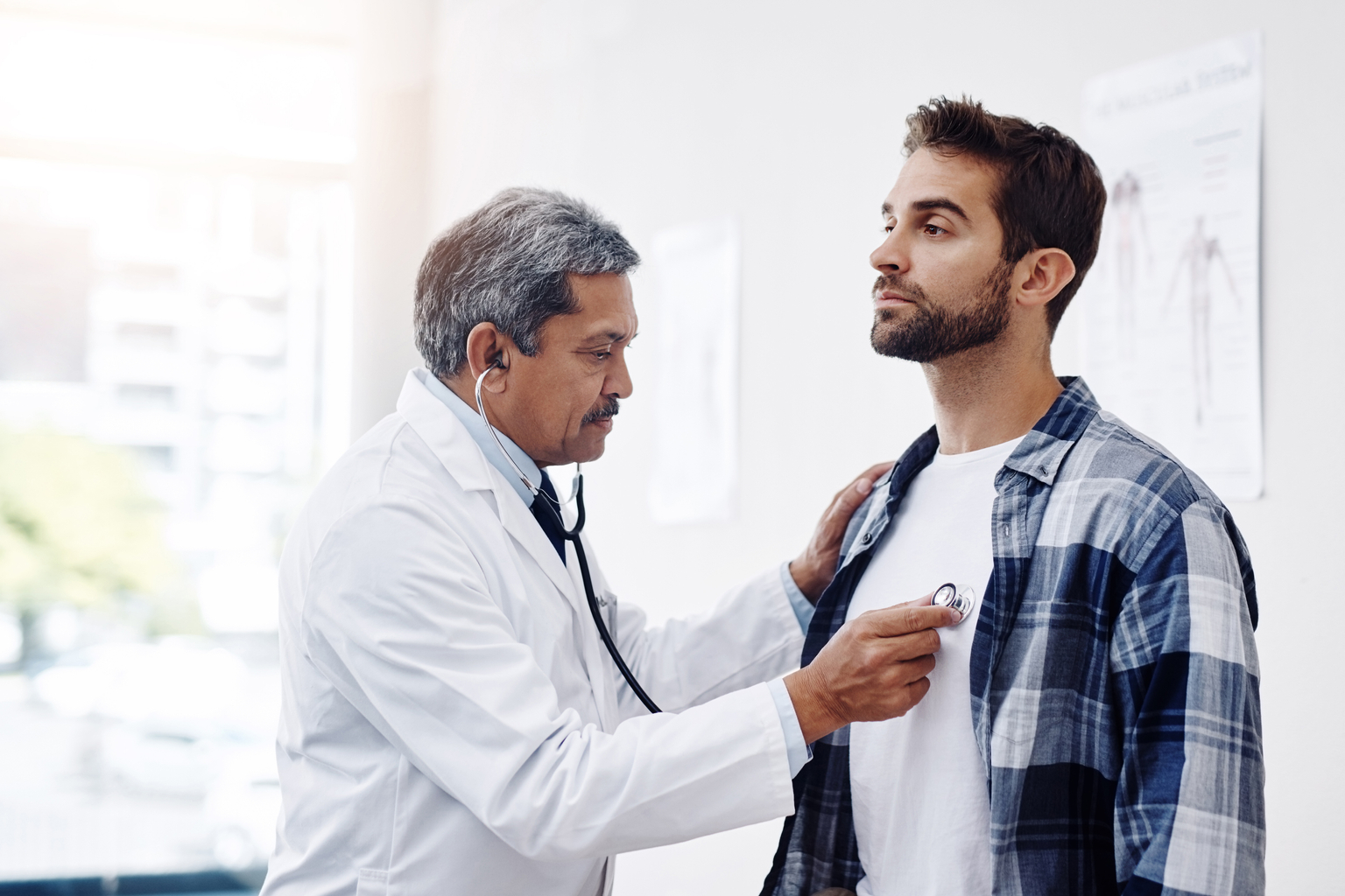 Male doctor examining male patient with a stethoscope in a clinic