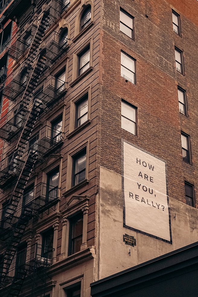 A high rise residential build with a sign on the side: How are you, really?