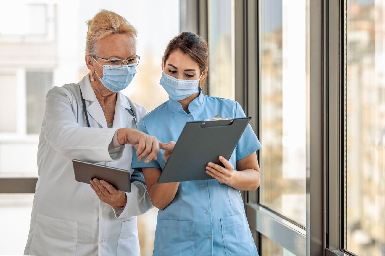Doctor and nurse in medical masks, conferring over clipboard and tablet