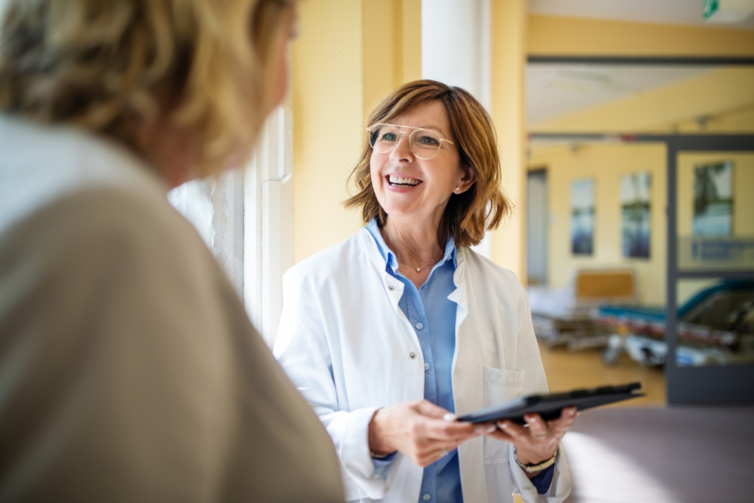 Mature female doctor with tablet talking to a female patient at hospital.