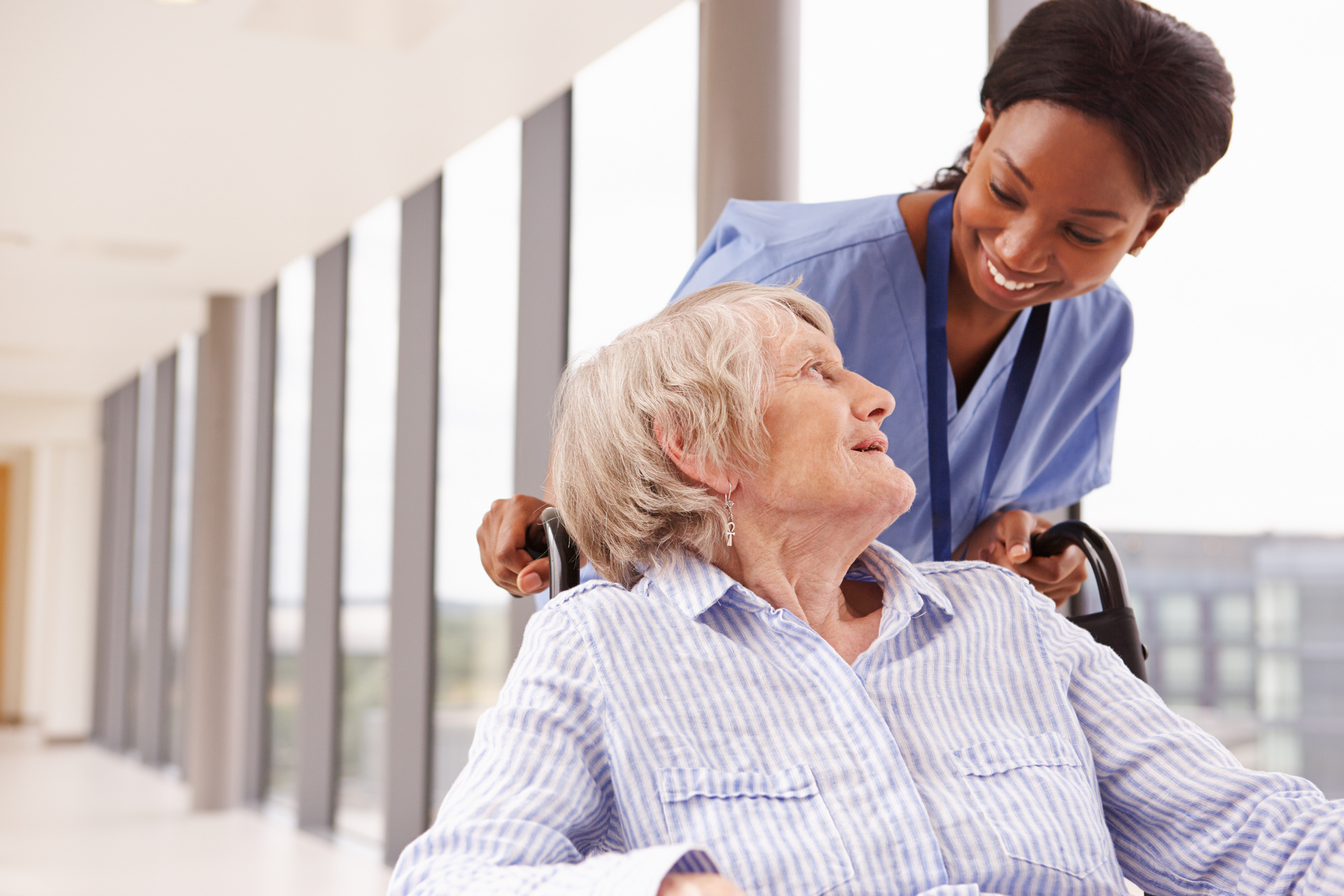 Nurse pushing senior patient in wheelchair along corridor