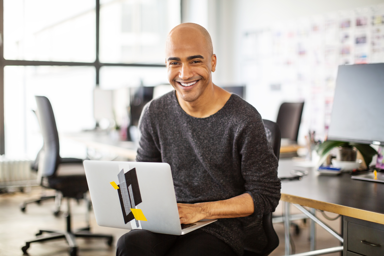 Mature businessman sitting by his desk with a laptop. Businessman with a laptop in office looking at camera and smiling.