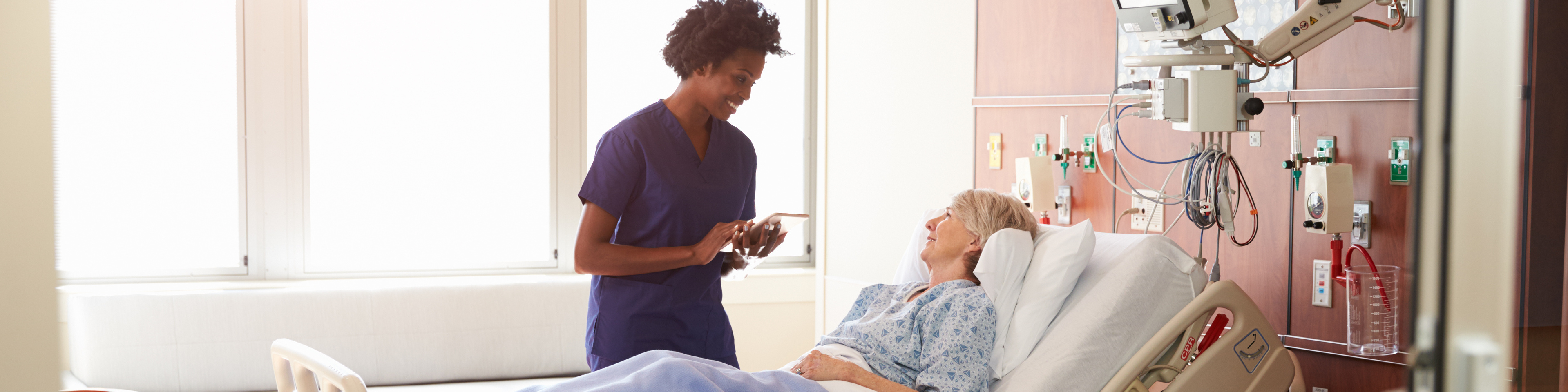 Hospital Nurse With Digital Tablet Talks To Senior Patient