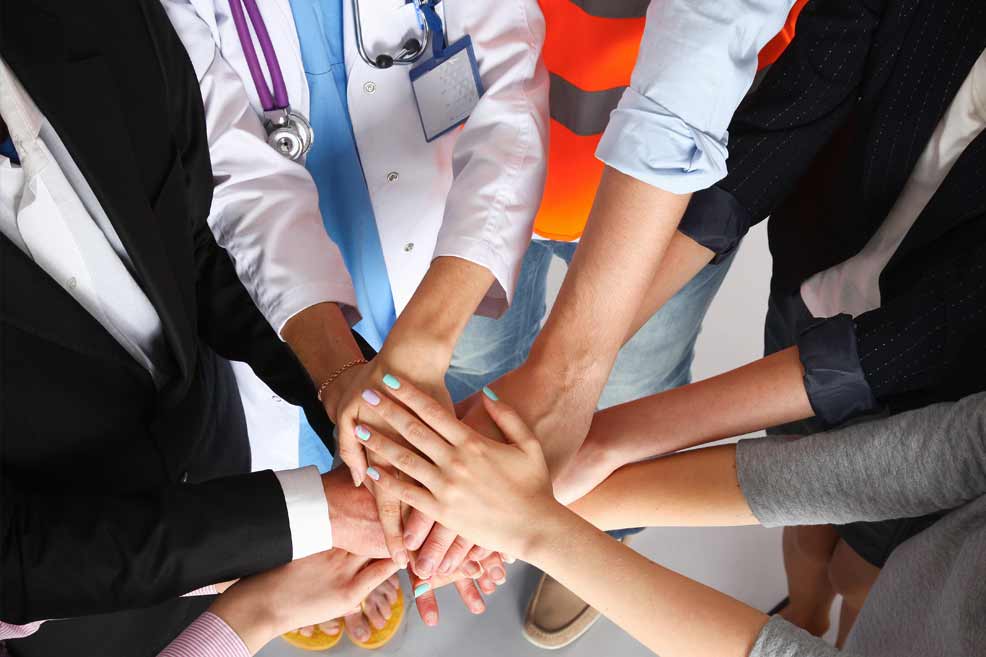 Various types of healthcare workers and staff putting their hands together in the middle