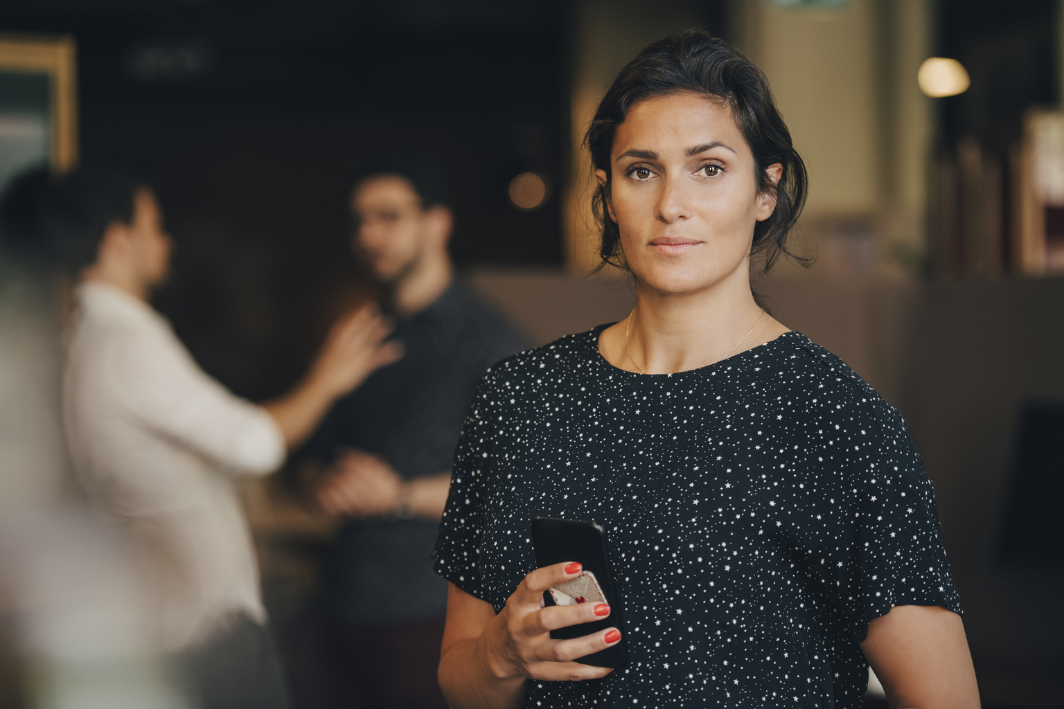 Portrait of confident businesswoman holding mobile phone in creative office