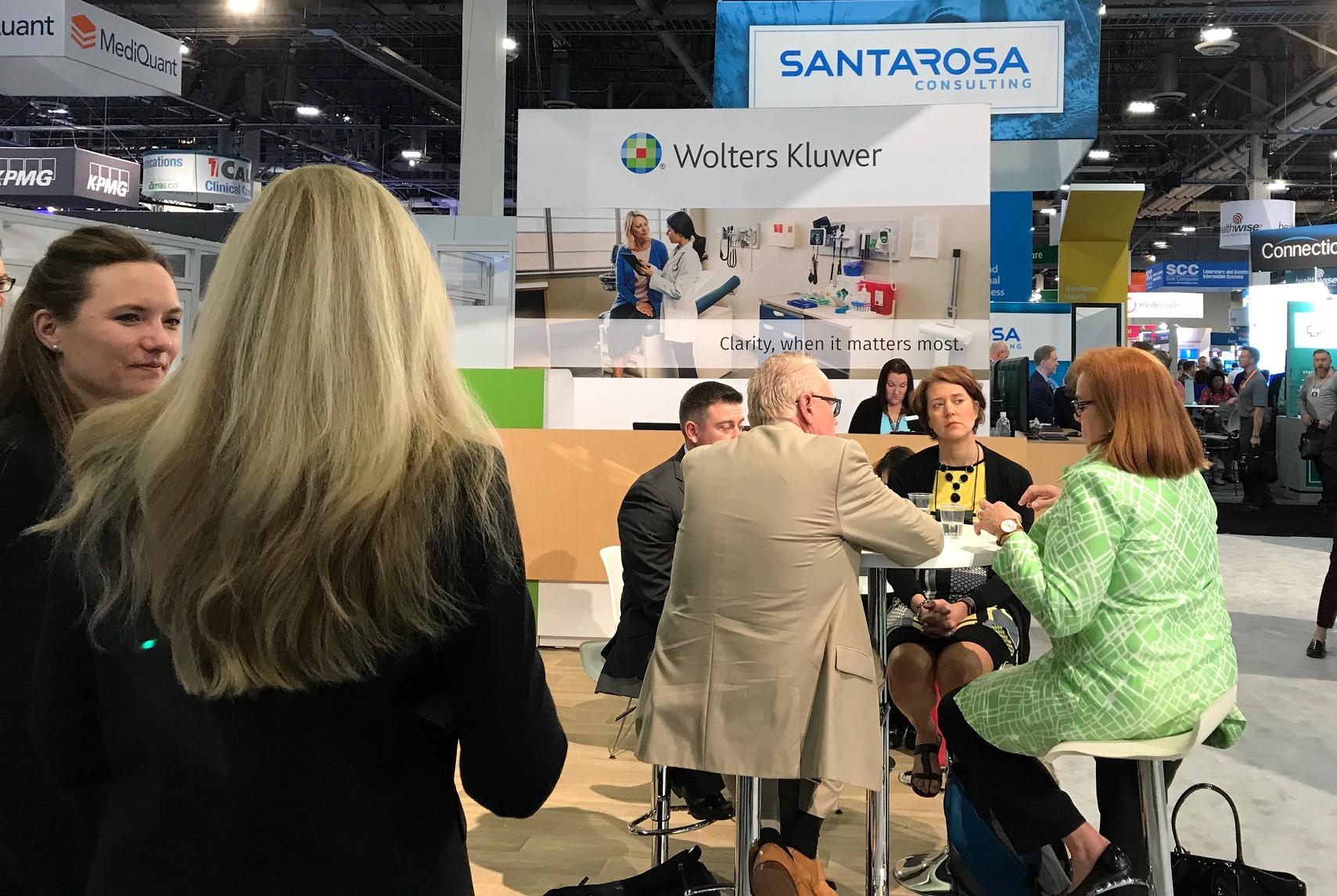 Groups of people gather at the Wolters Kluwer booth at the HIMSS conference.