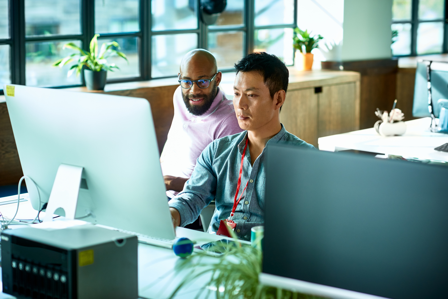 Asian male computer programmer working with African male colleague in office.