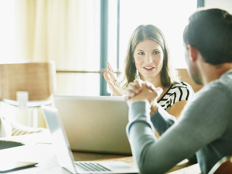 Smiling businesswoman in discussion with colleague at office conference room table.