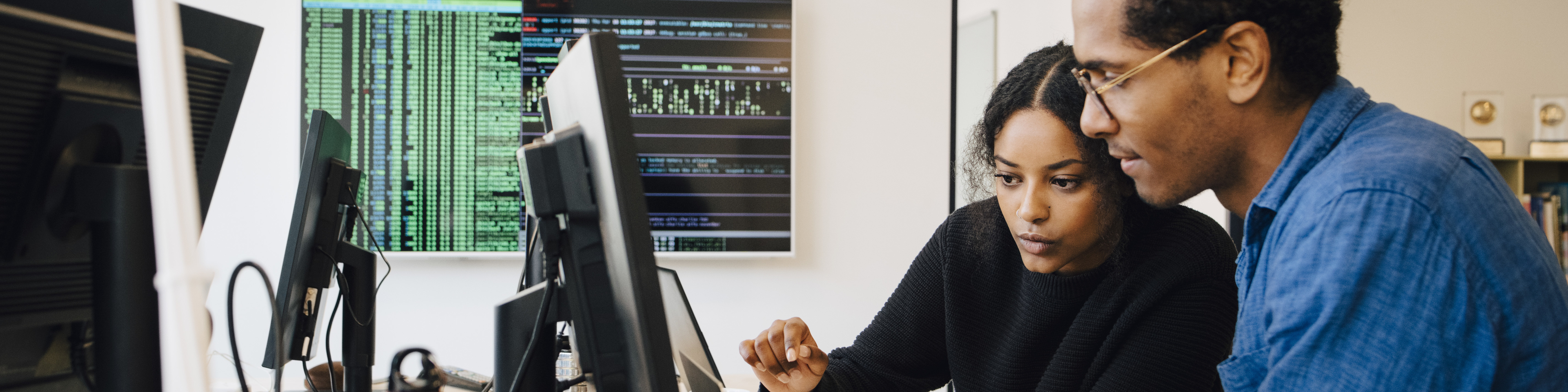 Focused male and female engineers coding over laptop on desk in office