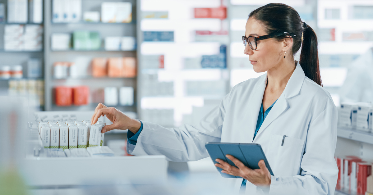 Female pharmacist uses digital tablet computer, checks inventory of medicine, drugs, vitamins, health care products on a shelf