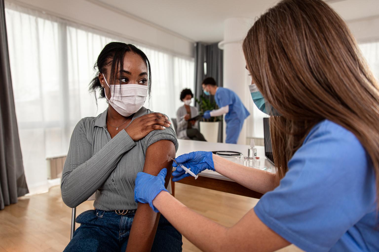 Nurse administering vaccine to diverse patient, wearing facemasks
