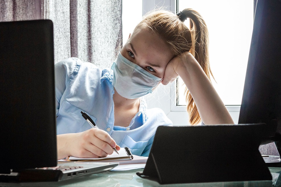 Female student wearing a face mask looking at computer screen and taking notes