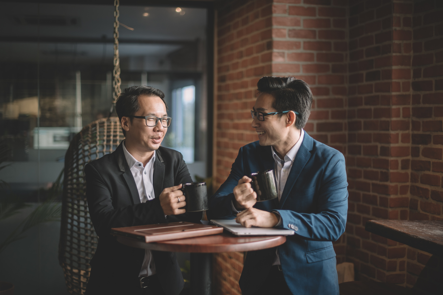 2 asian chinese white collar workers having discussion during their coffee break in lounge using laptop and digital tablet