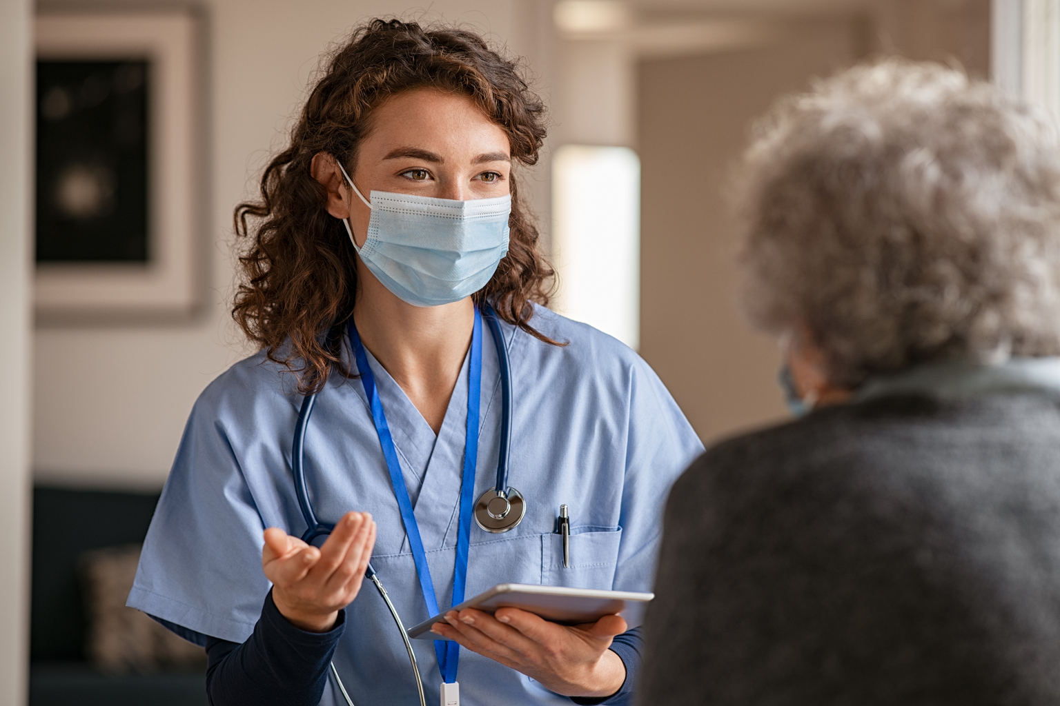 Young doctor visits senior woman with surgical mask.