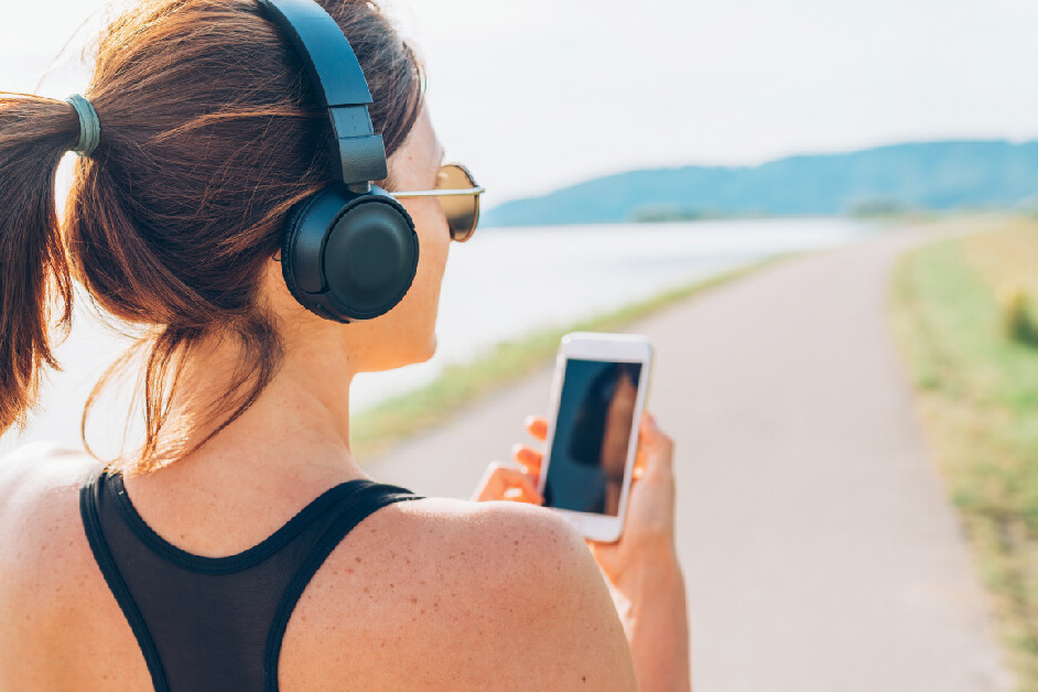 Young female walking on a path with headphones and iPhone