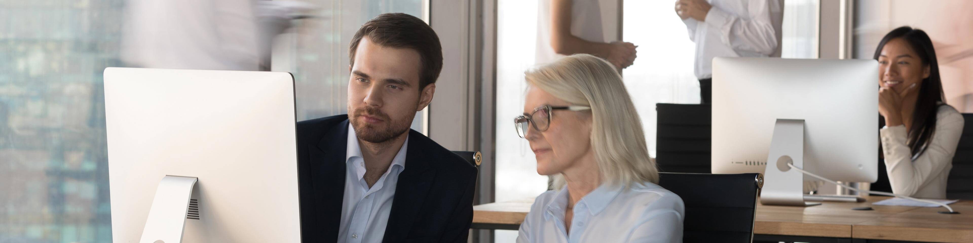 man and woman in business casual attire looking at an iMac.