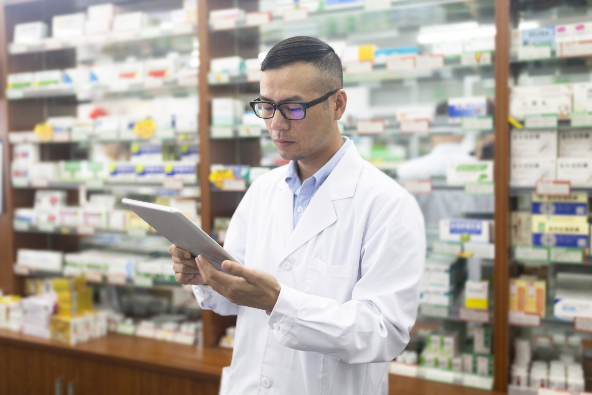 Young male Asian doctor works on a tablet at a pharmacy.