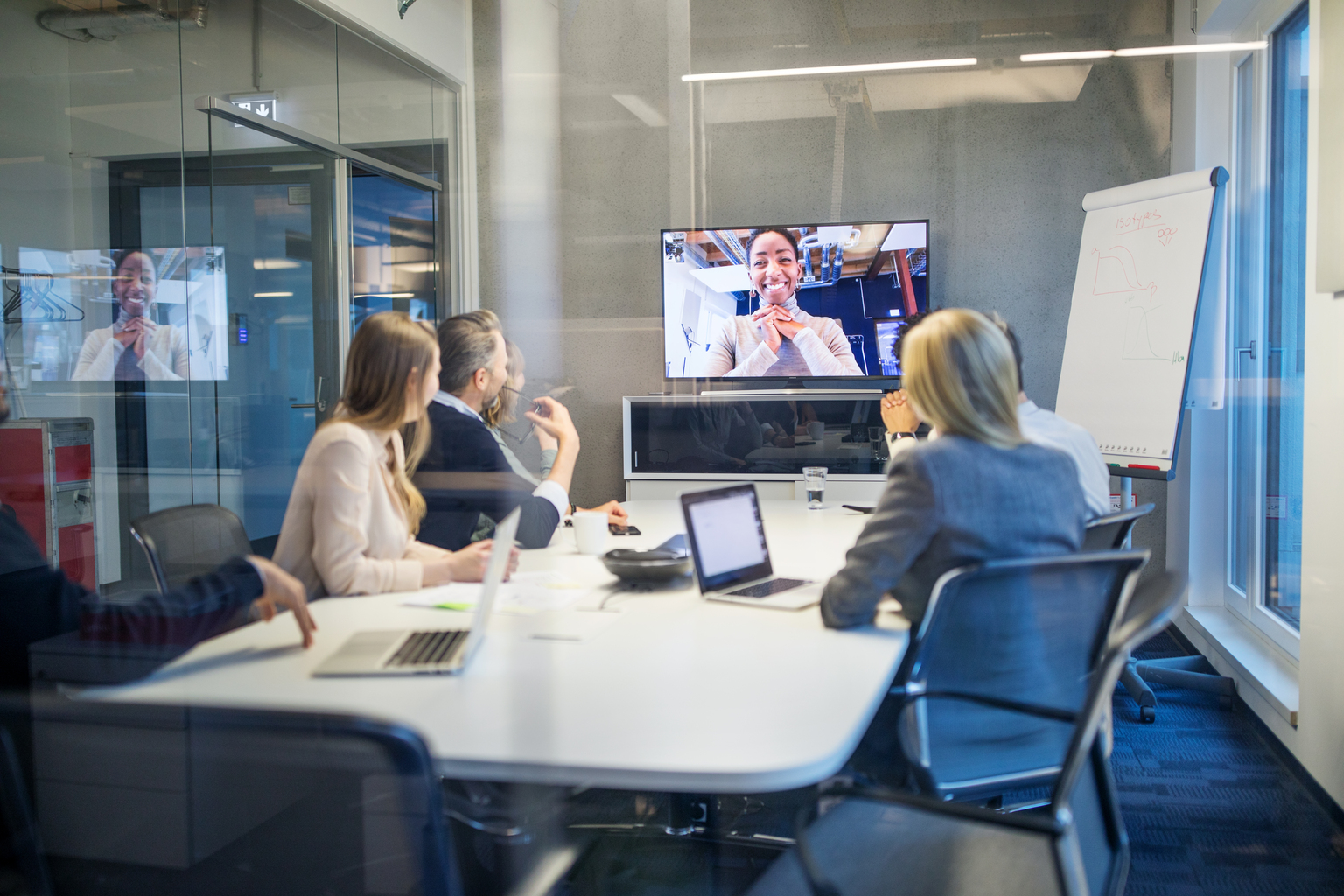 Business people looking at a screen during a video conference in the office. Businesswoman having video conference meeting with team sitting in board room