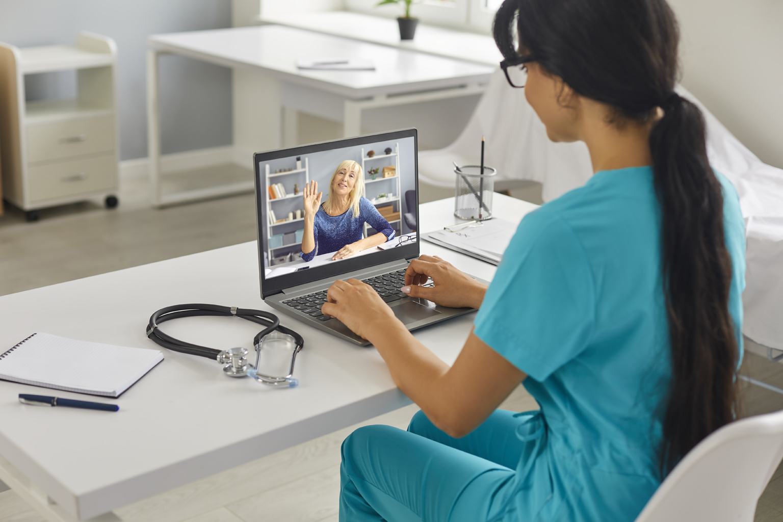 Healthcare worker sitting at desk on laptop with patient, telemedicine/telehealth