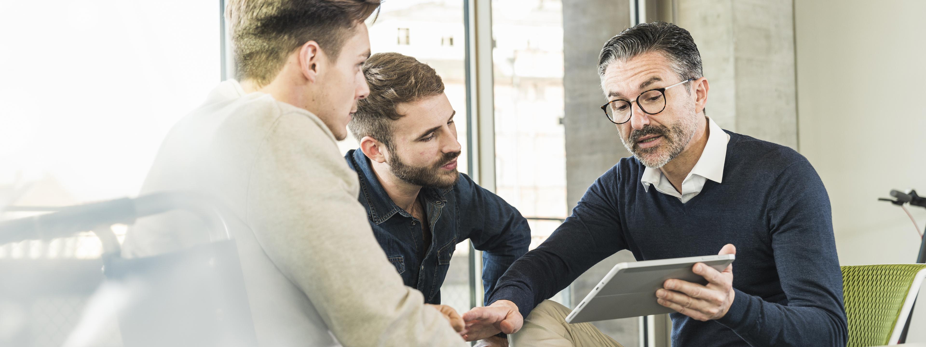 Three businessmen having a meeting in office sharing a tablet