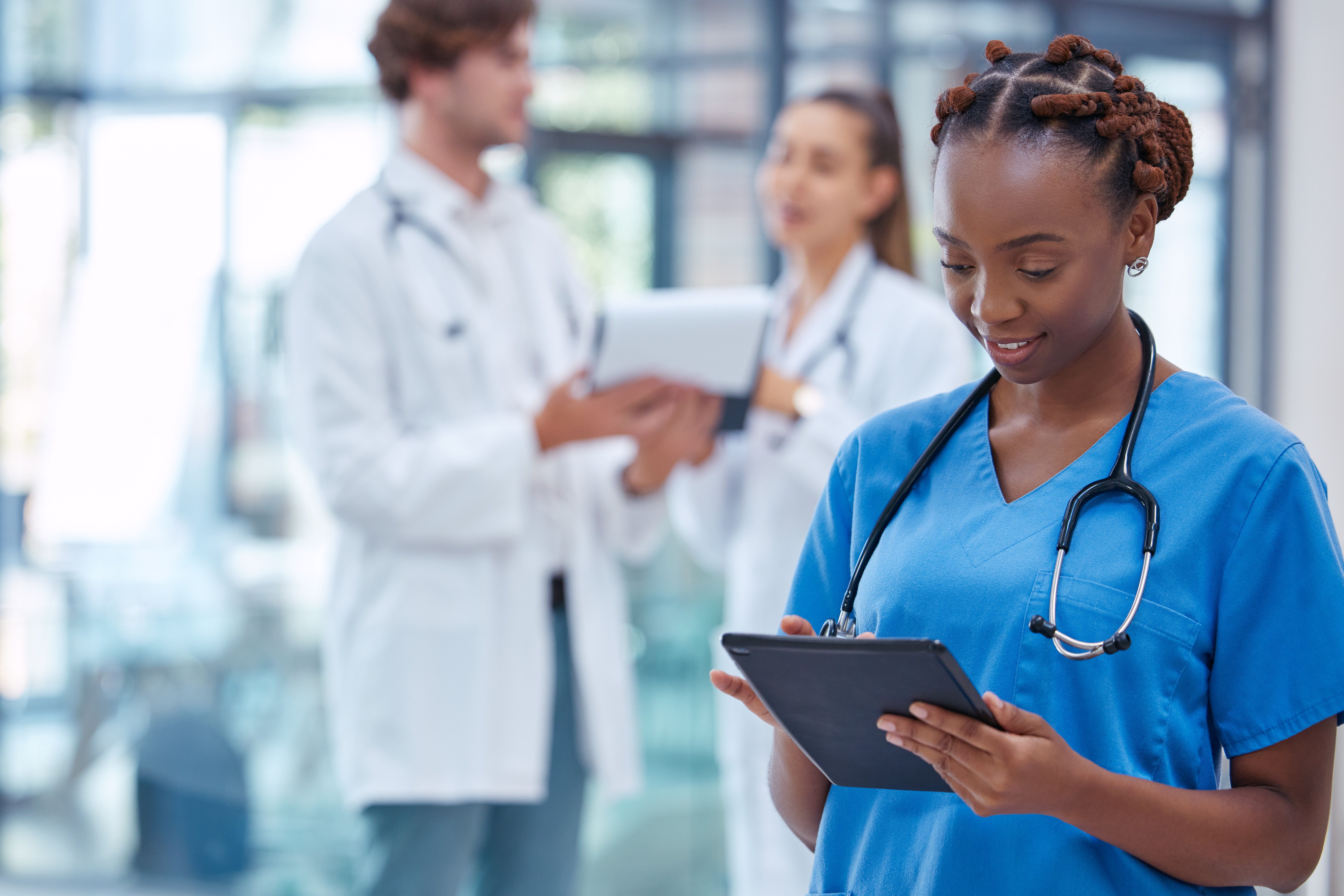 Medical professional wearing scrubs, using tablet to record patient data. 