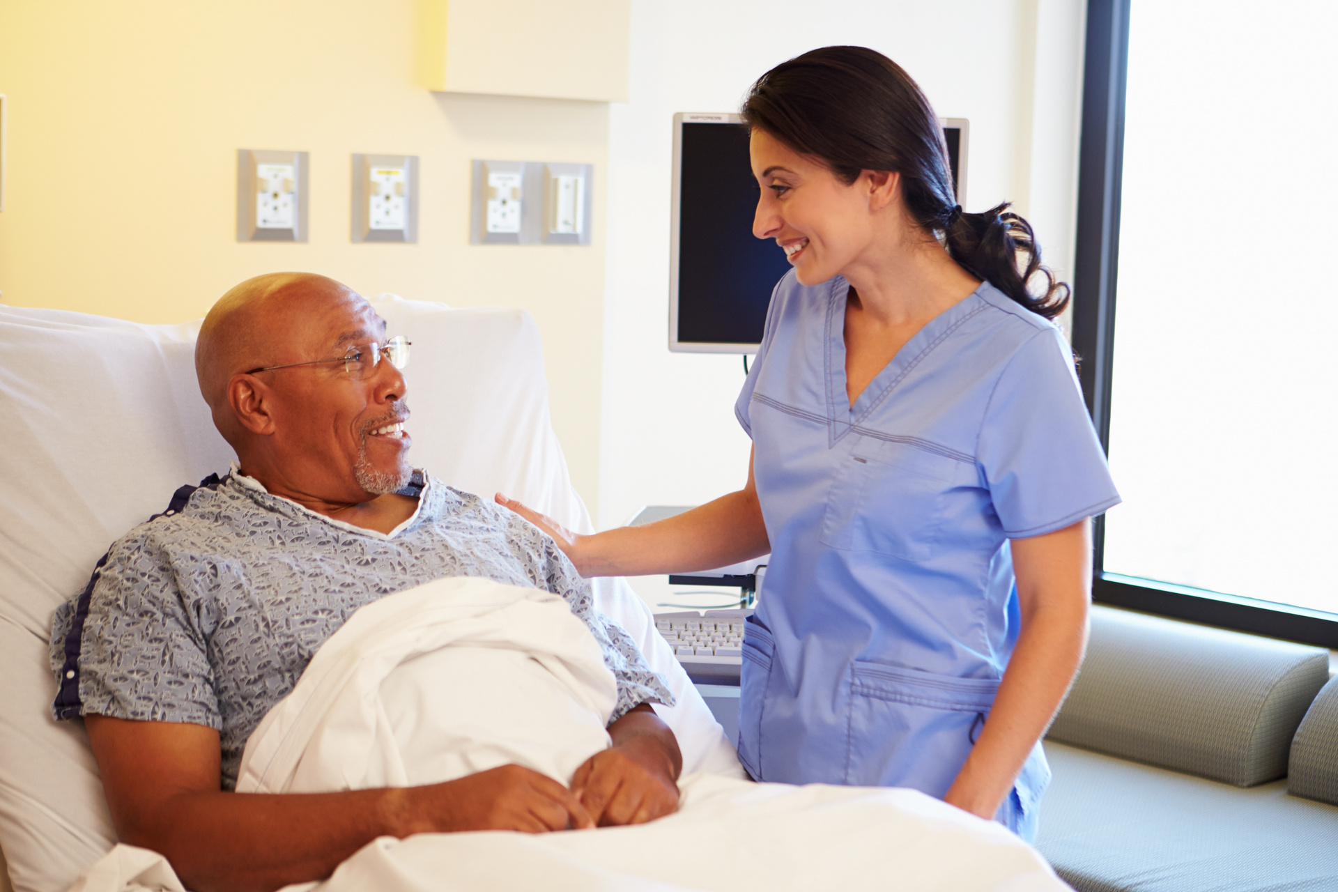 Nurse in blue scrubs at patients bedside providing care