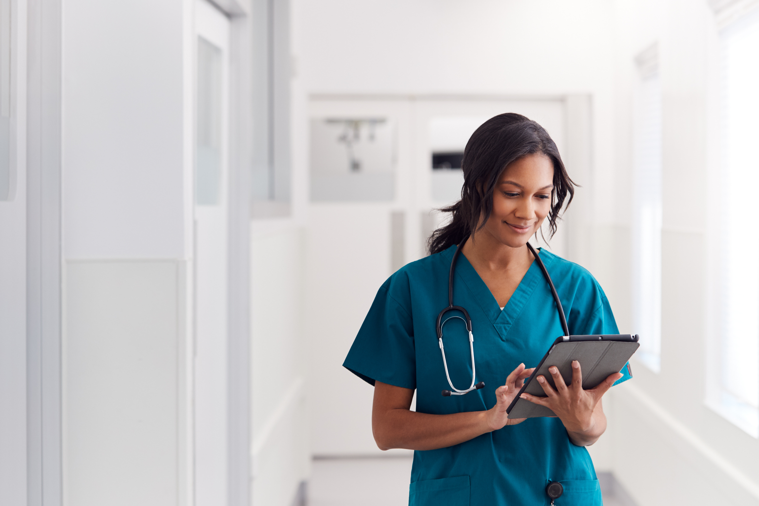 Nurse in hospital hallway reading on a tablet device