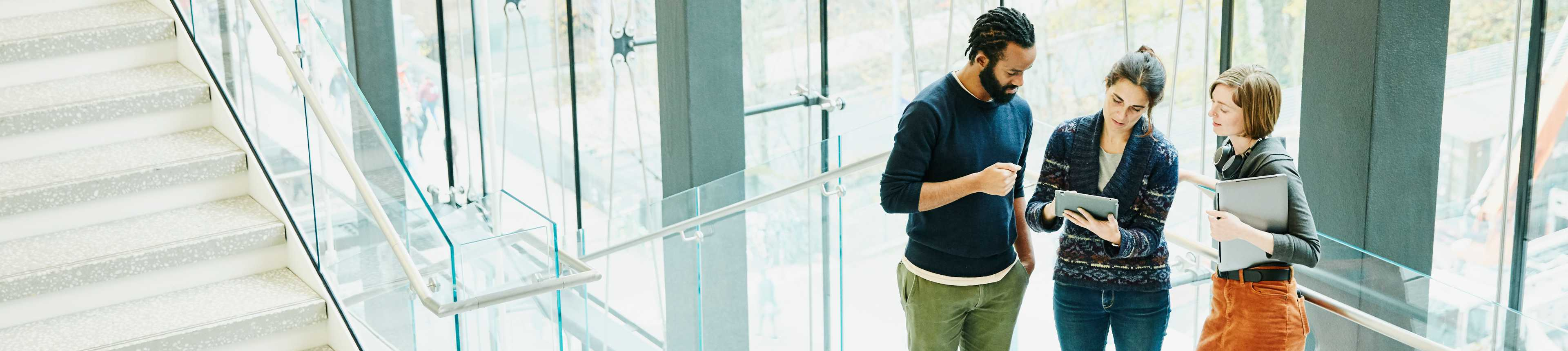 Man and two women reviewing tablet in office stairway