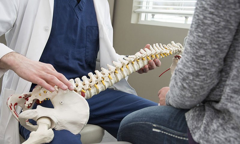 A doctor speaking to a patient over a model of a spine