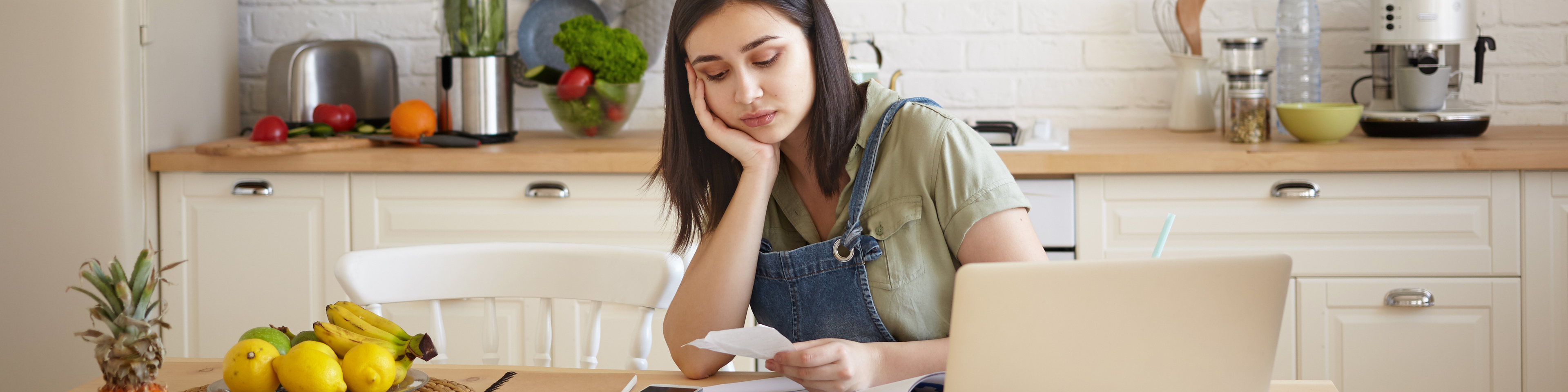 Woman sitting at kitchen table, doing paperwork and calculating budget