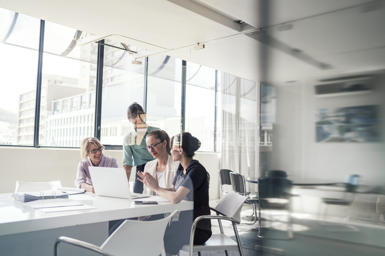 A photo of multi-ethnic businesswomen discussing over laptop in office. Female professionals are in formals. Executives are in meeting at brightly lit workplace.