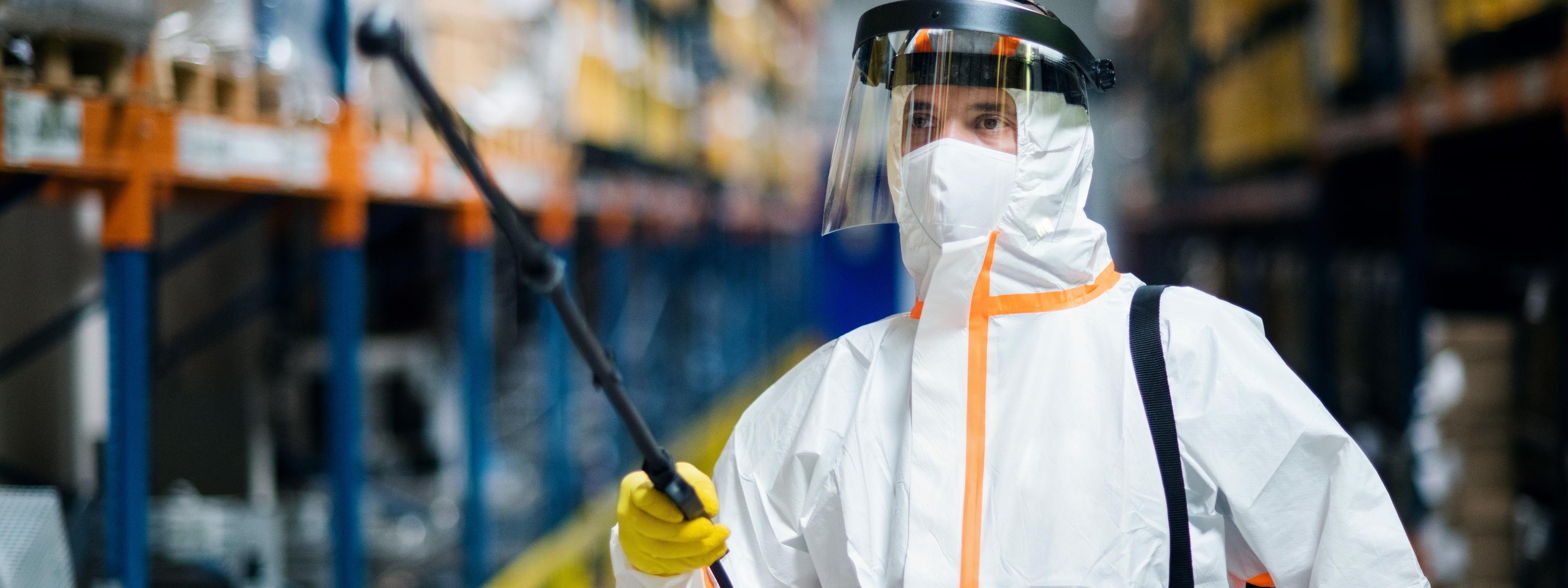 Man worker with protective mask and suit disinfecting industrial factory with spray gun.