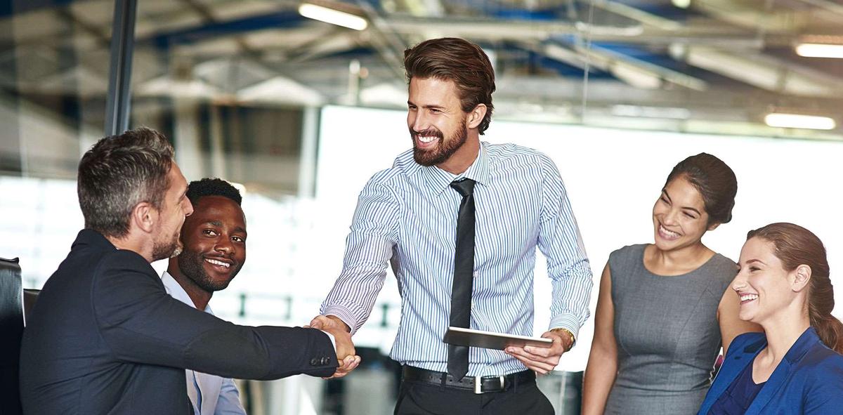 Professionals meeting and shaking hands while holding a tablet with TeamMate's audit management software.