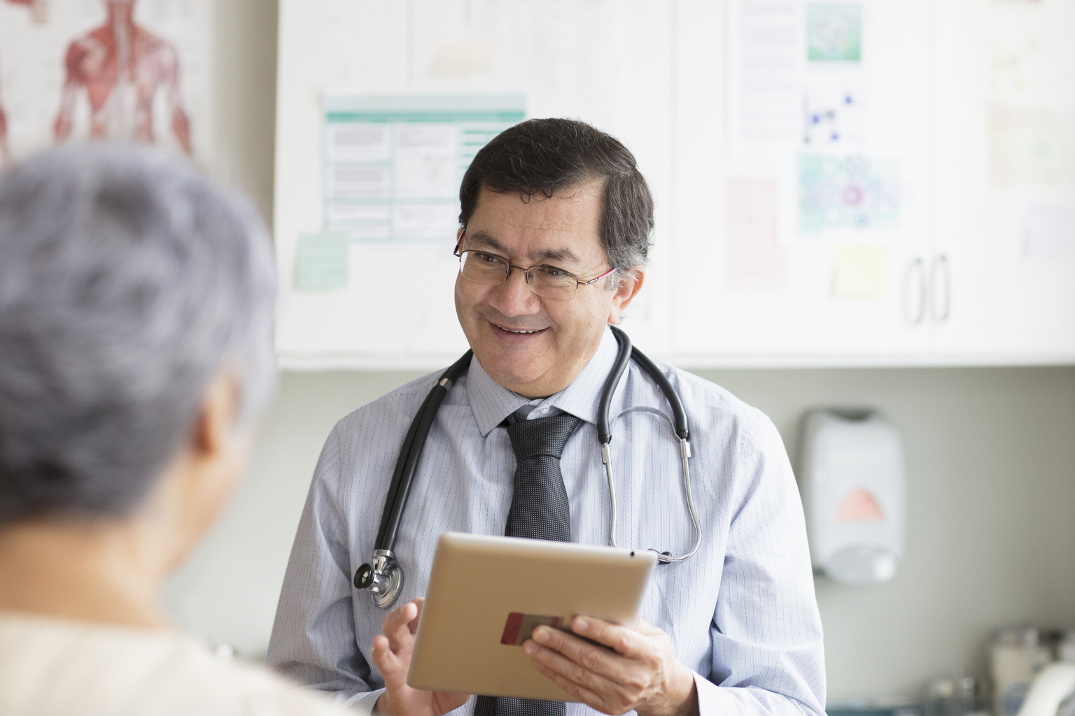 Hispanic male doctor with digital tablet talking to patient.