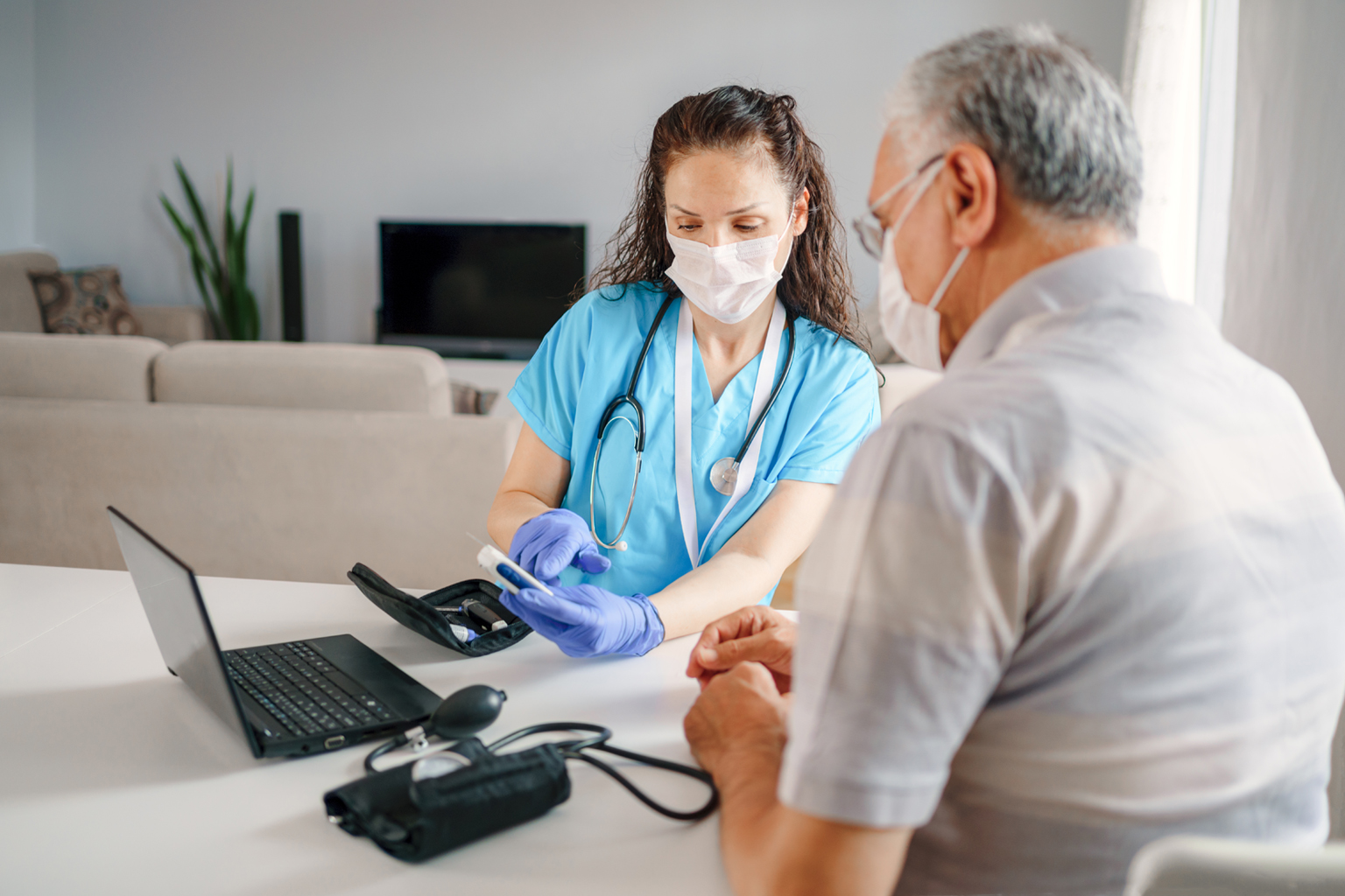 Nurse sitting with older male, both wearing masks, looking at results of some test