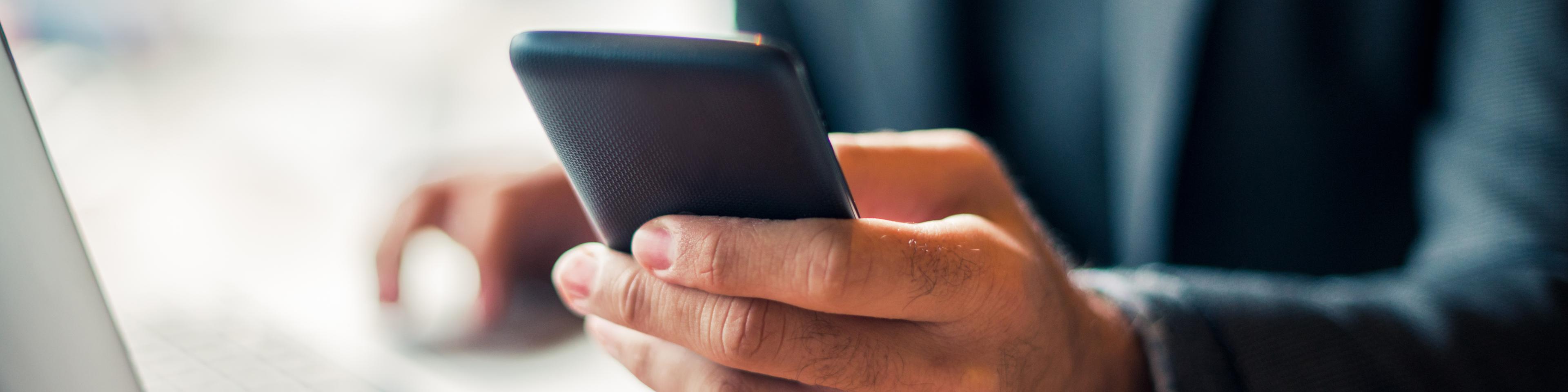 Man with Navy blue business suit holding his smart phone and using his laptop touchpad, Q3 2021, TAA NA US - Preparer