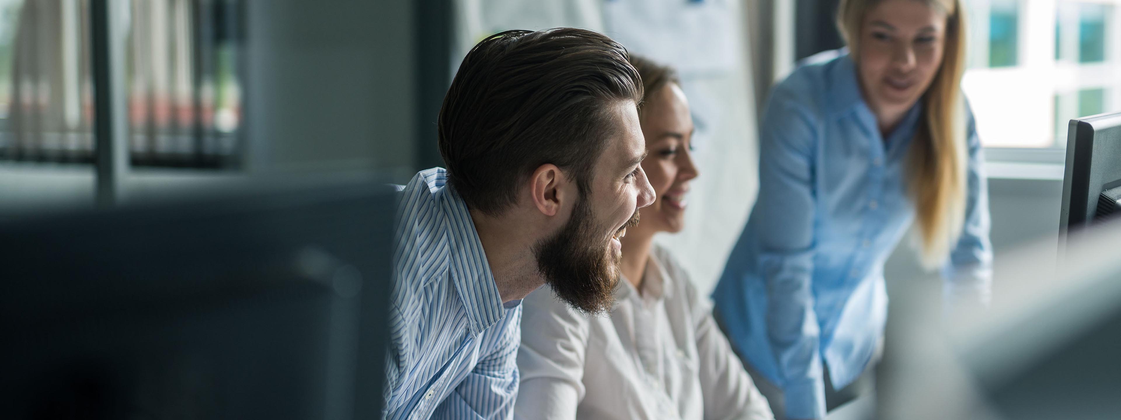 man with beard and two woman behind desk looking at computer