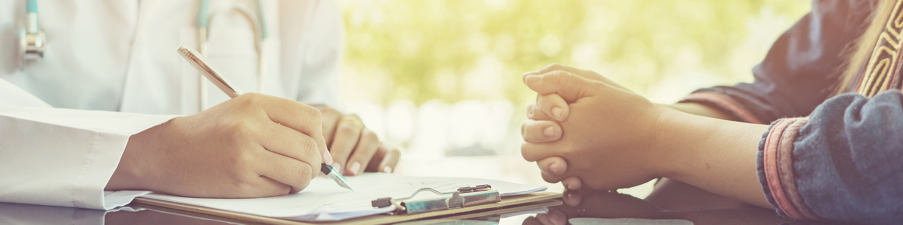 Close up on doctor writing notes and sitting with patient at desk